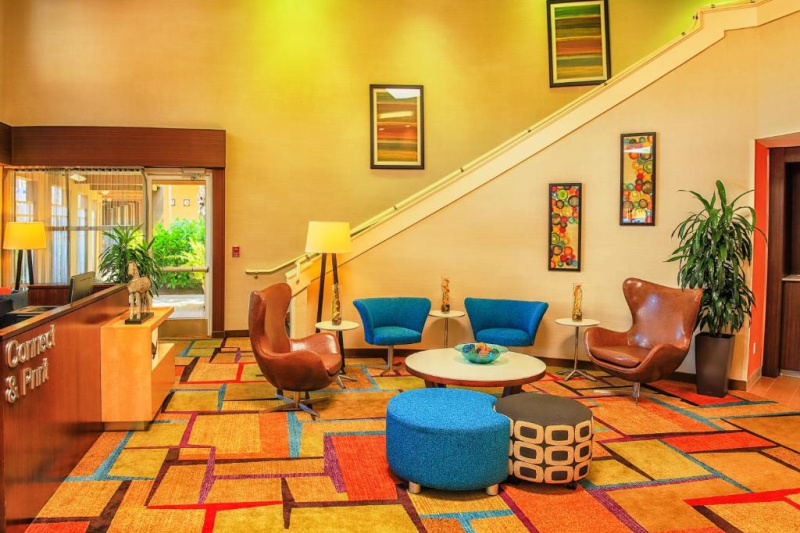 The connect and print area has a high counter. There is a seating area with assorted low tables and movable chairs and pouffes. Stairs with handrails lead up to the next floor.