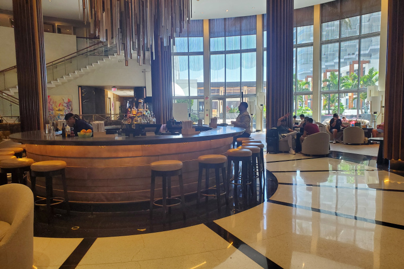 The bar is large and circular with bar stools around it. There are seating areas and a flight of stairs leading down to it.