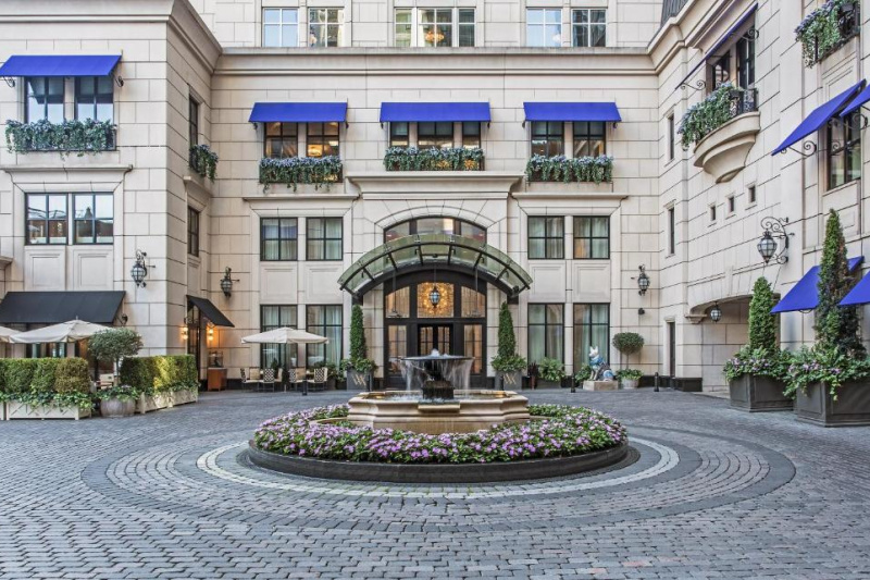 Exterior view of the hotel entrance. There is a brick-paved driveway around a circular fountain in front of the main doors.
