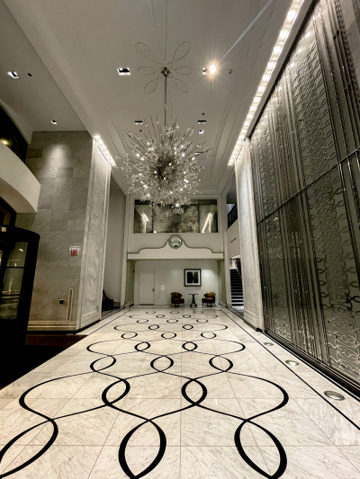 The spacious, airey step-free lobby has a seating area with a table and 2 armchairs next to a flight of stairs leading to the next floor. There is an exit sign with a push button on the wall by the revolving entrance doors.