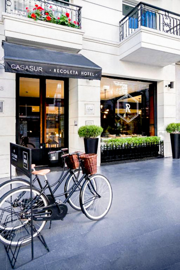 The entrance to the hotel is from the sidewalk through a tall glass door. The hotel bicycle stand is outside the hotel entrance.