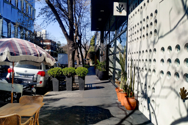 The hotel entrance is from the sidewalk. Outside the hotel there is a table and 2 chairs with a sun canopy. There are also potted plants.