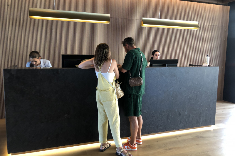 The reception desk has a high counter with 2 large computer monitors. The surrounding area has a smooth wooden floor.