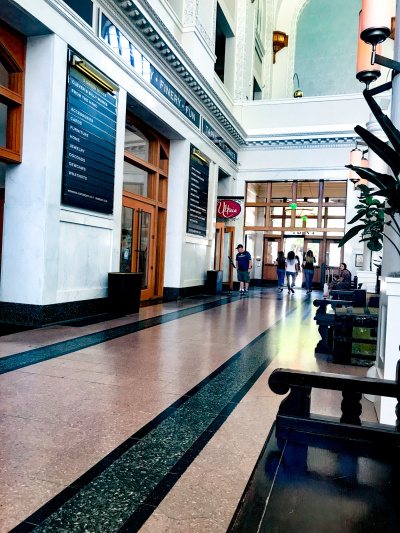 The spacious hotel lobby is lined with shops, bars and wooden benches.The exit is through 2 wooden and glass doors.