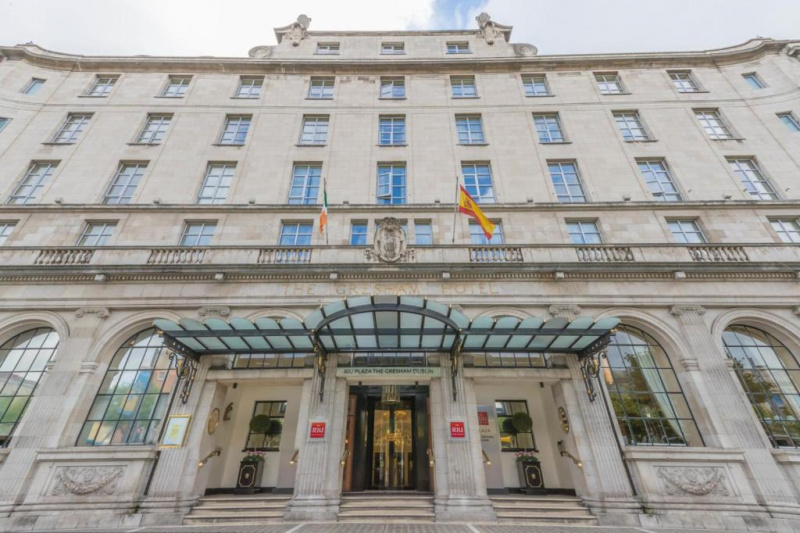 The hotel is a 5-story, classical building. There are 3 steps with handrails leading up to a sliding glass door.