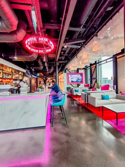 The brightly lit bar has a high counter and bar stools around it. There is a seating area with sofas across a spacious aisle.