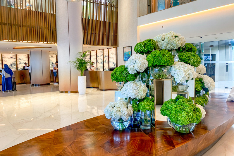 The spacious lobby area has high reception desks. In the lobby there is a long, low wooden table with a flower arrangement on it.