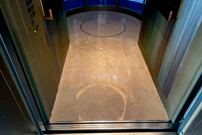 The glass elevator has 2 handrails and accessible call buttons.