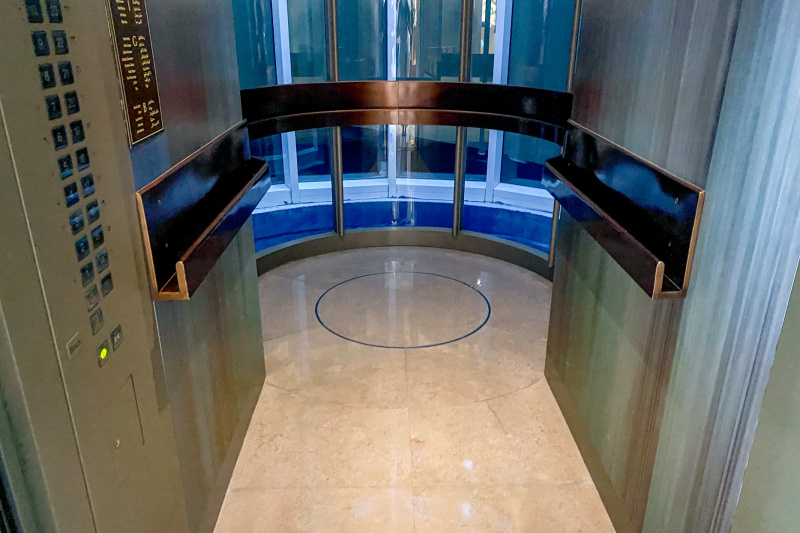 The glass elevator has large display buttons and has a handrail on all sides.
