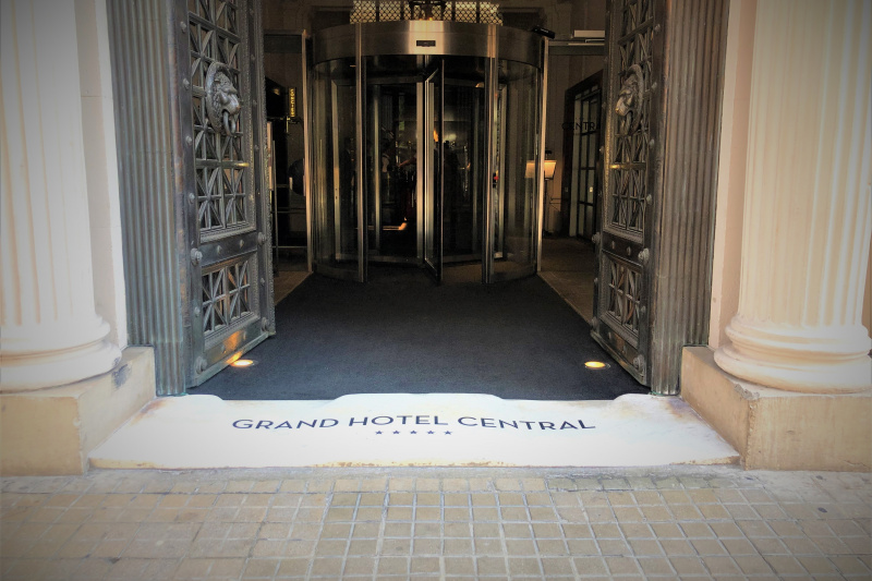 Access to the hotel from the sidewalk is through 2 wrought iron doors leading to a revolving door with an automatic glass door on one side.