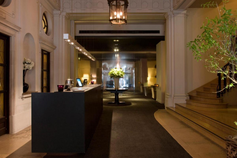 The spacious hotel lobby has a waist-high concierge service desk. There are two steps leading to a flight of marble stairs with a handrail.