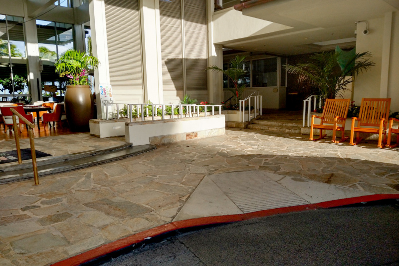 There is a dropped kerb with a tactile strip leading to a crazy paving area. To the left there are two wide, shallow steps with a handrail leading to The Veranda. To the right there are 2 steps with handrails leading to Hoku's. There is access to a shallow ramp with handrails leading to The Veranda.