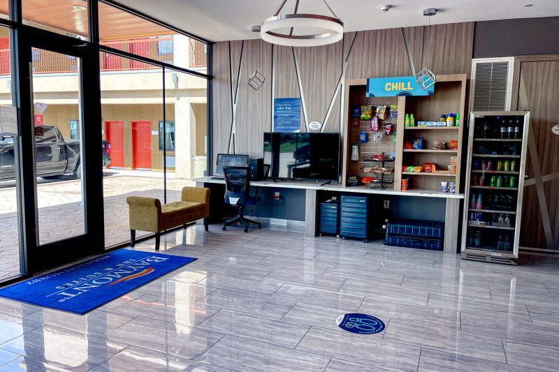 The spacious lobby has a computer, a TV, shelving with snacks, and a refrigerator with drinks. There is also a padded bench and a movable chair