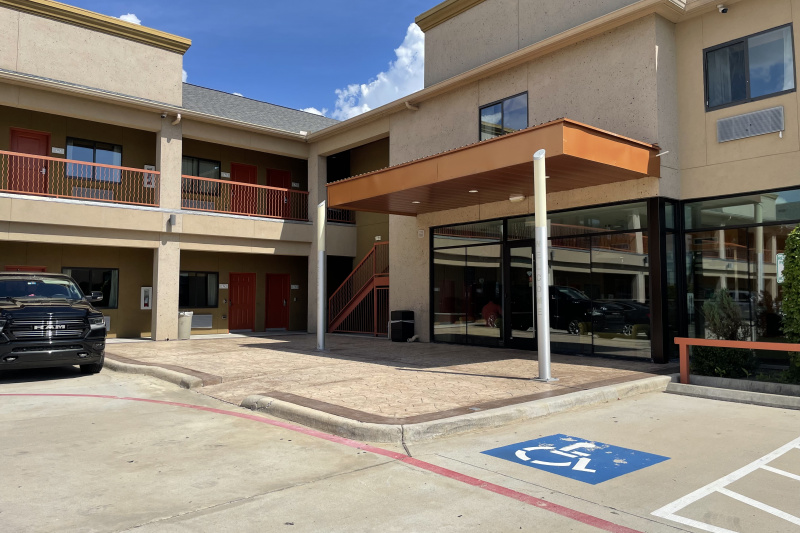 An external view of the hotel has accessible parking. There is a small ramp leading to a paved area.