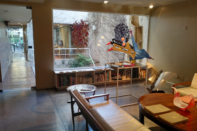 The seating area has a sofa, an armchair, and 3 assorted tables. There is a shelving unit with books. Outside there are stairs with handrails leading to a lower floor.