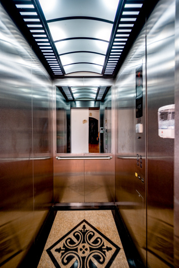 The elevator is narrow with a handrail along the end. The call buttons are accessible.