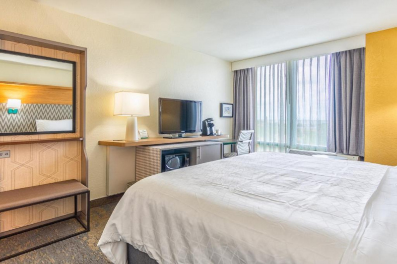 The room has a king-sized bed. There is a table opposite with a TV, a cupboard with microwave and mini-fridge beneath, and a desk with coffee machine and chair.