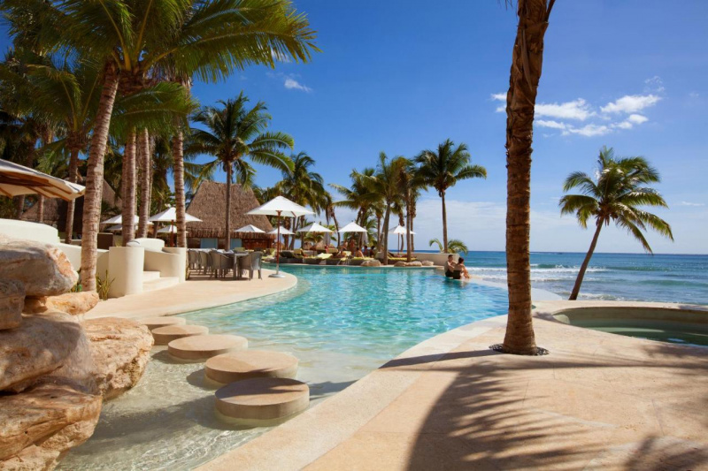 The outdoor swimming pool has steps leading down to it.There is a stepping stone bridge in the pool and round the poolside there are movable tables and chairs.