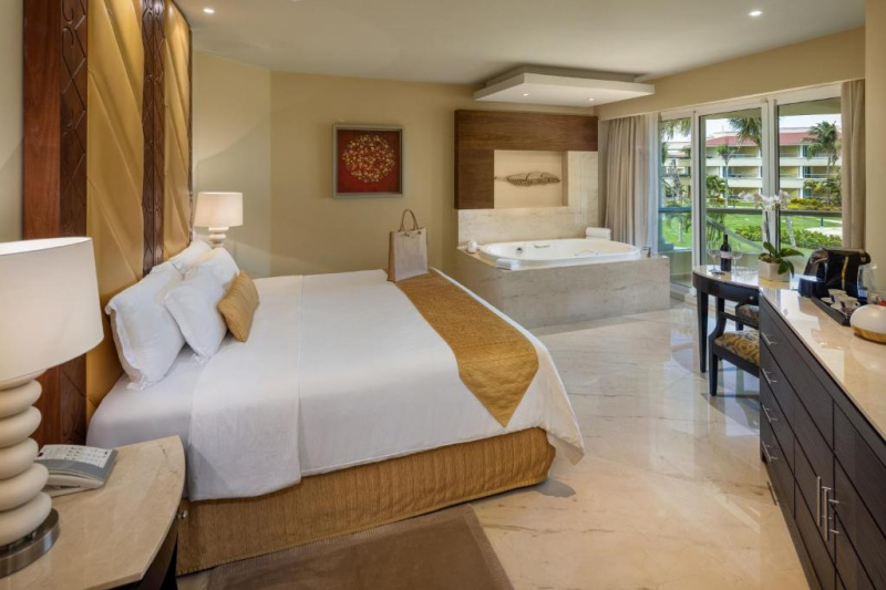 The ground-floor accessible room has a king-sized bed with nightstands, table, chair, and sideboard. There is a double whirlpool bathtub to one side.