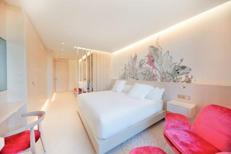 The step-free, spacious hotel room has a seating area with plush chair and footstool next to a king-sized bed with nightstands. There is a workstation with movable chair opposite. The ensuite is screened off.
