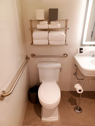 The restroom has 2 grab bars, a low paper dispenser and an accessible sink. There is a wall-mounted towel rack above the cistern.