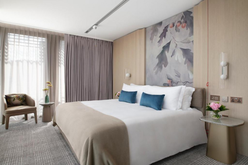 The spacious room has a king-sized bed with nightstands, an emergency pull cord, armchair, table, and floor-to ceiling windows.