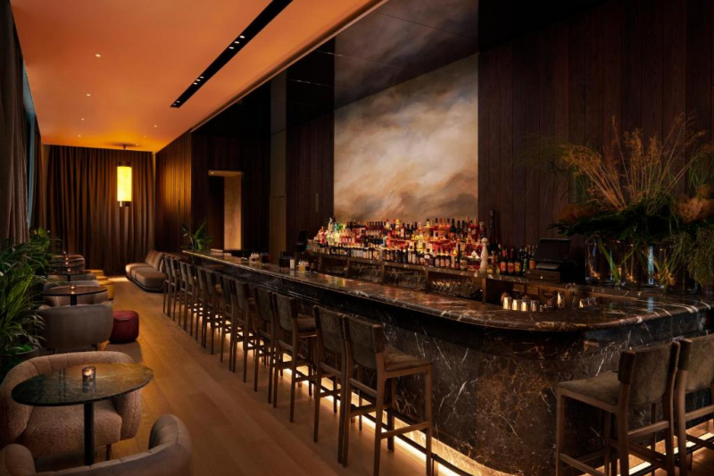 The well-stocked bar has a high counter lined with bar stools. An aisle separates the bar from a row of tables and armchairs.