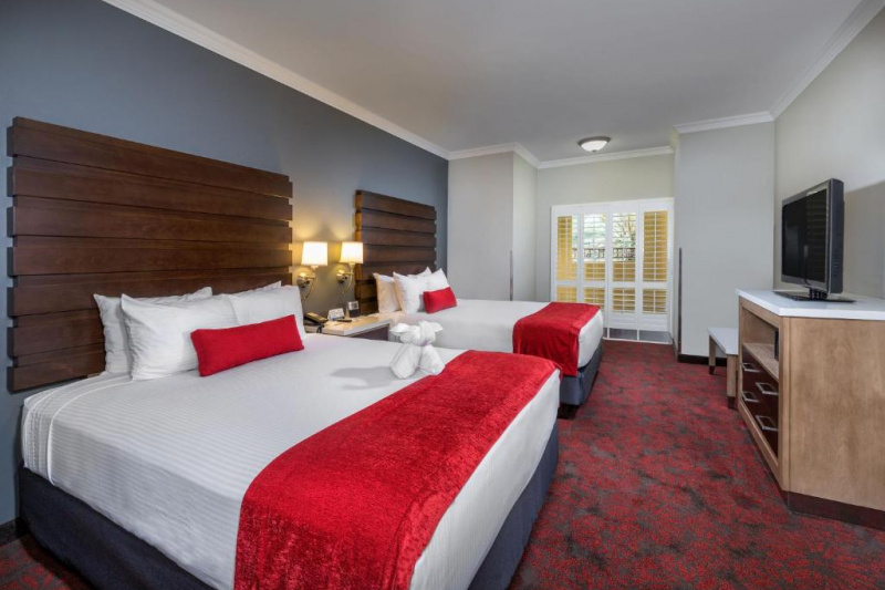 The carpeted twin room has a central nightstand. There is a chest of drawers opposite the beds with a TV on top.