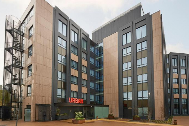 An exterior view of the Urban hotel in the Corendon Village complex. There is a fire escape to the left and a designated parking area.