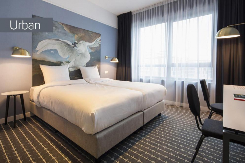 The spacious room in the Urban Hotel has 2 twin beds pushed together with nightstands, wall-mounted reading lamps, and a workstation with 2 movable chairs.