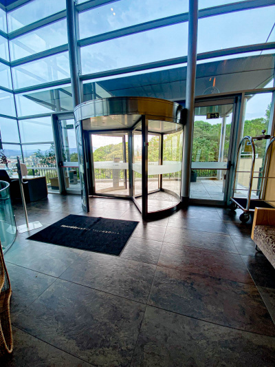 A revolving door with a glass door on either side provide step-free access from the spacious lobby to the terrace outside. There is a large doormat in front of the revolving doors.