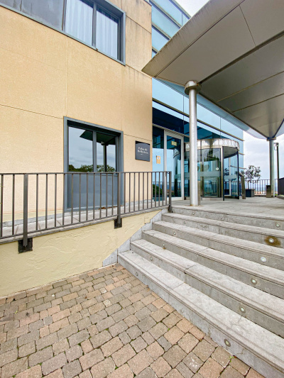 A ramp runs along the hotel wall and next to a flight of 6 steps, both leading to a covered terrace in front of the revolving door of the hotel entrance.