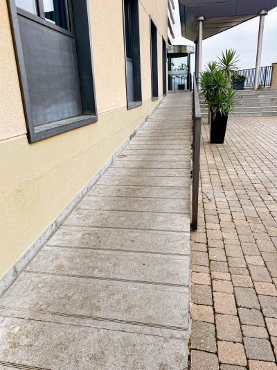A long, shallow, narrow ramp leads to a covered terrace in front of the revolving door of the hotel entrance.