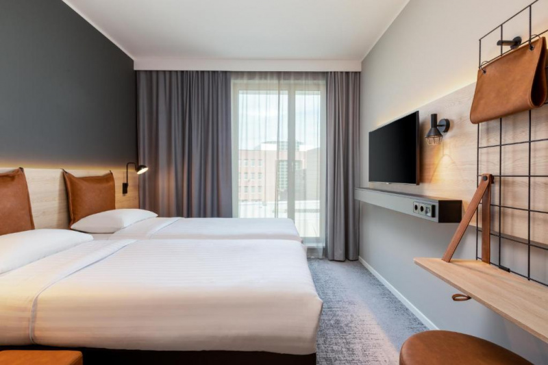 The room has 2 twin beds, a fold-down shelf unit, wall-mounted TV and a floor-to ceiling window. There is limited floor space.
