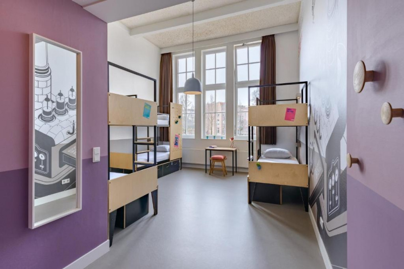 This dorm room has 3 sets of bunk-beds and small desk and a stool.