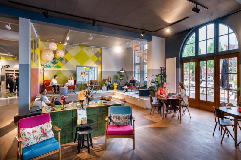 The hostel lobby has a seating area with assorted tables, movable chairs and a sofa.There are 2 small stairs leading to a raised platform where there are more tables and chairs.
