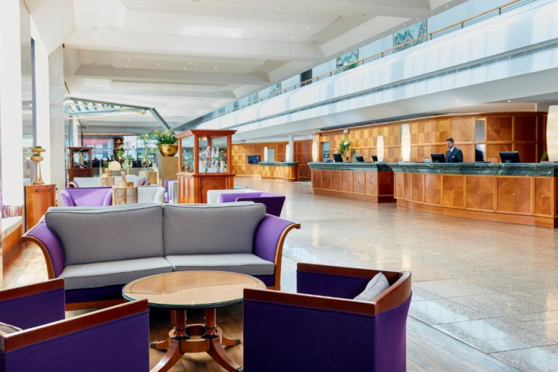 The spacious hotel lobby has 2 high check-in desks, a concierge desk and a seating area with sofas, chairs and coffee tables.