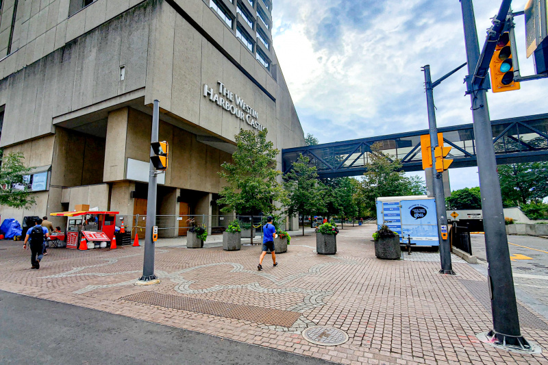 External view of the hotel, which is a large, concrete building on the corner of a spacious step-free, brick-paved sidewalk. There is also an aerial covered walkway to the hotel.