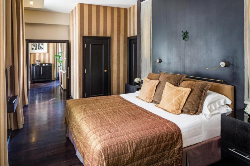 The spacious room has a king-sized bed with nightstands, a TV, and double doors leading to the living room.