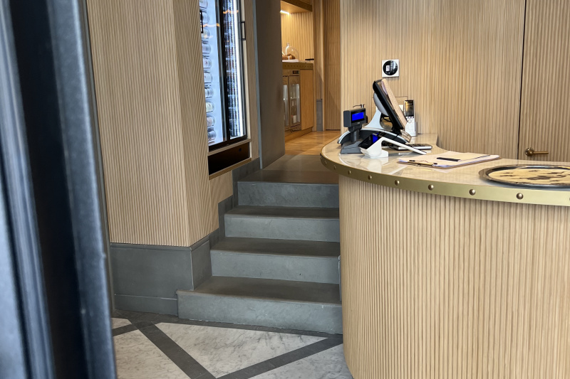 The check-in desk has a high counter. A flight of 4 steps leads past a built-in vending machine to a mini-fridge and food counter.