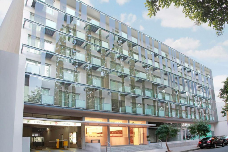 The hotel is a large, modern, 5-story building. There are steps with handrails leading up to the hotel and a carpark at the side.
