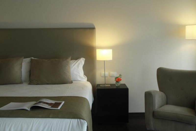 This hotel room has a bed with a nightstand next to it. There is an armchair beside the nightstand.