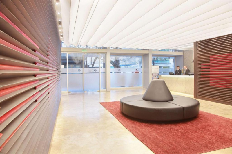 The lobby is spacious and step-free. There is a circular chair in the middle of the room and the high reception desk is to one side of the room.