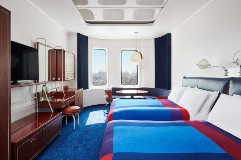This room has 2 full-sized beds with a workstation, movable chair, cupboards and wall-mounted TV opposite. The window has built-in seating with a table.