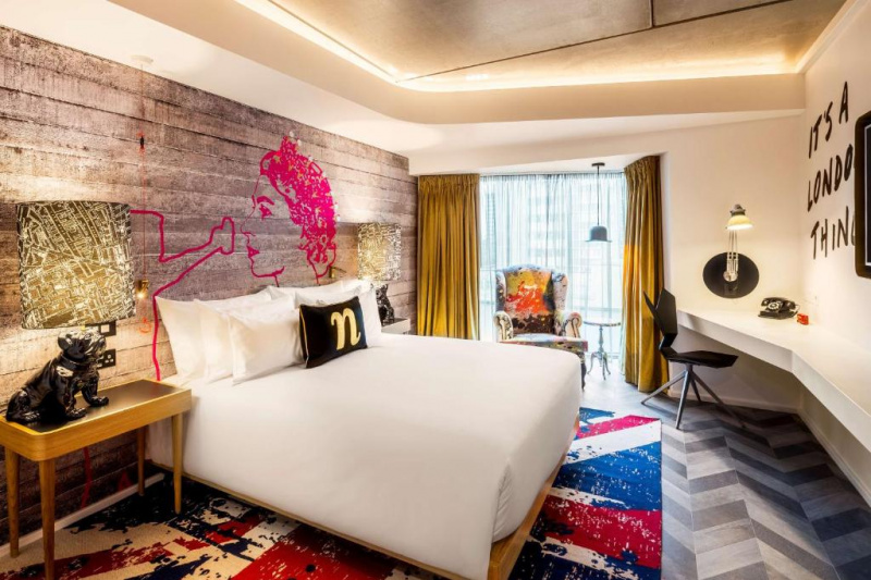 The room has 1 queen-sized bed with nightstands on either side. There is a high-backed armchair and built-in workstation.