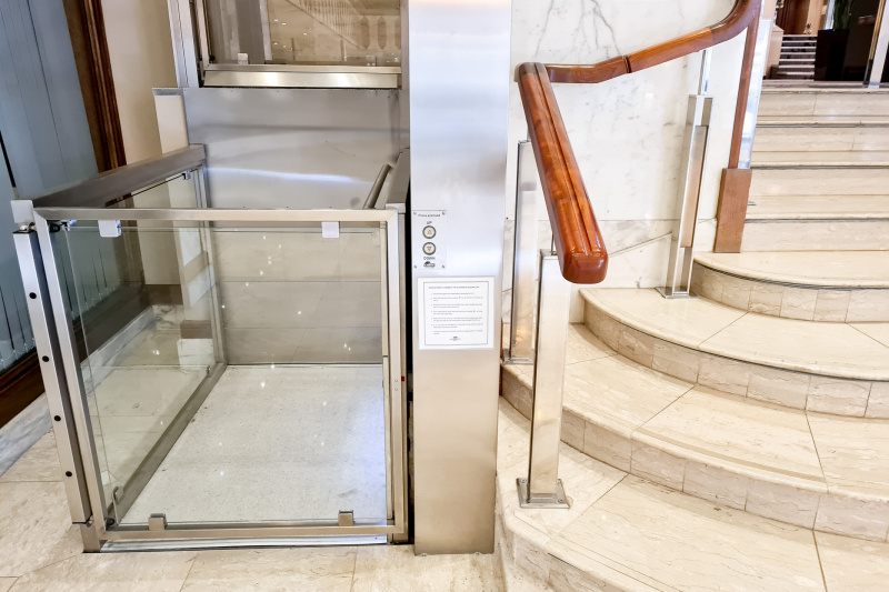There is a wheelchair lift next to a flight of stairs with a handrail leading to the next floor.