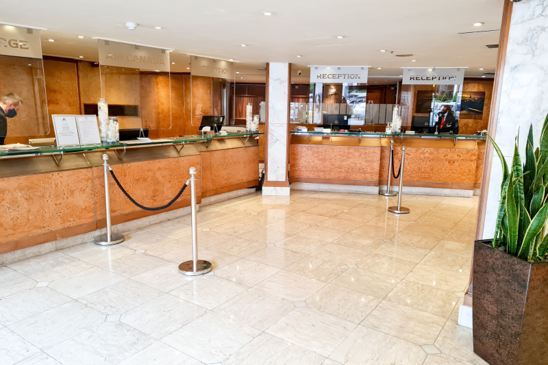 The spacious reception area has a long L-shaped check-in and concierge desk with plexiglass screens. There are also queue barriers.