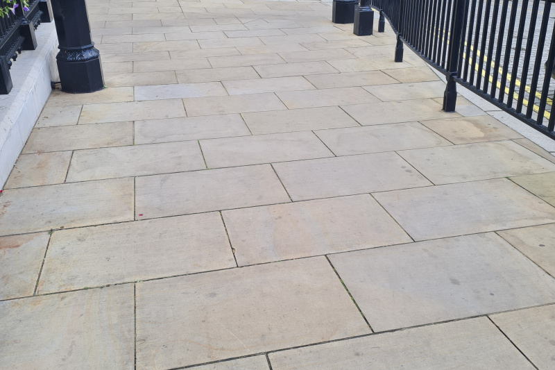 The sidewalk is very wide, step-free and paved. There is a railing to one side of the sidewalk.