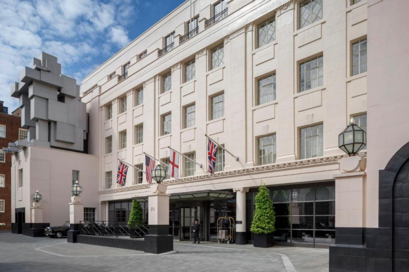An external view of the hotel from the sidewalk, which is a large Art Deco building. Access to the hotel is through a revolving door. There is a wide driveway leading up to the entrance.