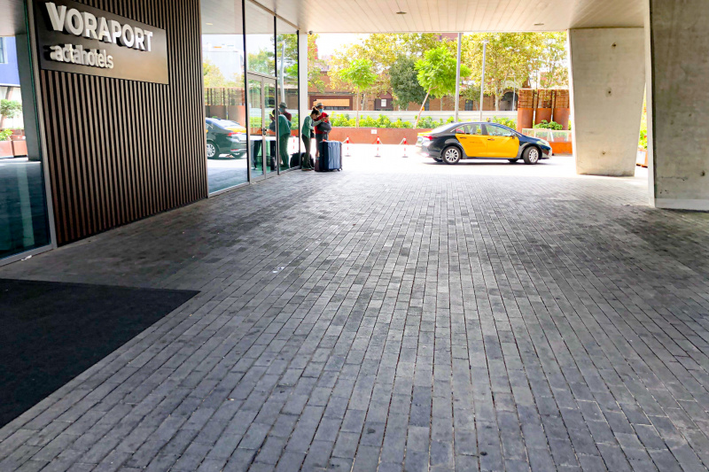 The hotel entrance is from a wide, covered driveway. There are glass doors that lead to the lobby.